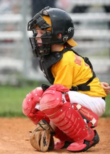 Image of a Youth 12 and Under Baseball Catcher in a yellow shirt, and red shin gaurds.