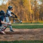 Fastpitch softball catcher in university uniform in a crouch behind home plate at an outdoor stadium